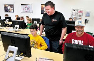 Brian Mulvey (standing), an instructor with Black Rocket Productions, watches as Chris Simonelli, 11, and his dad, Mike Simonelli of Frederick County, play a 2-D video game. (Photo by Ginger Perry/The Winchester Star)
